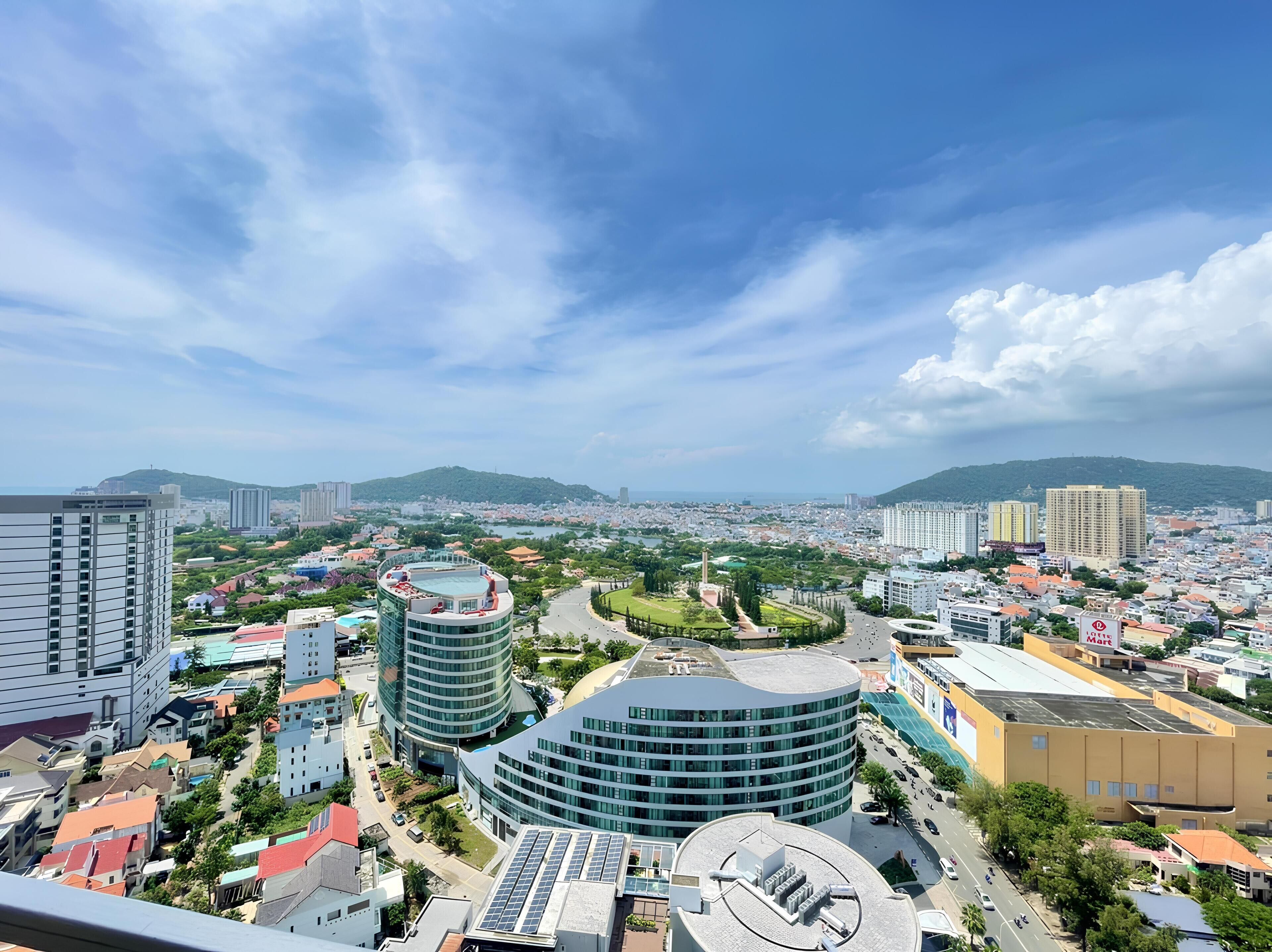 A cityscape with modern buildings, a roundabout, and a view of distant hills.