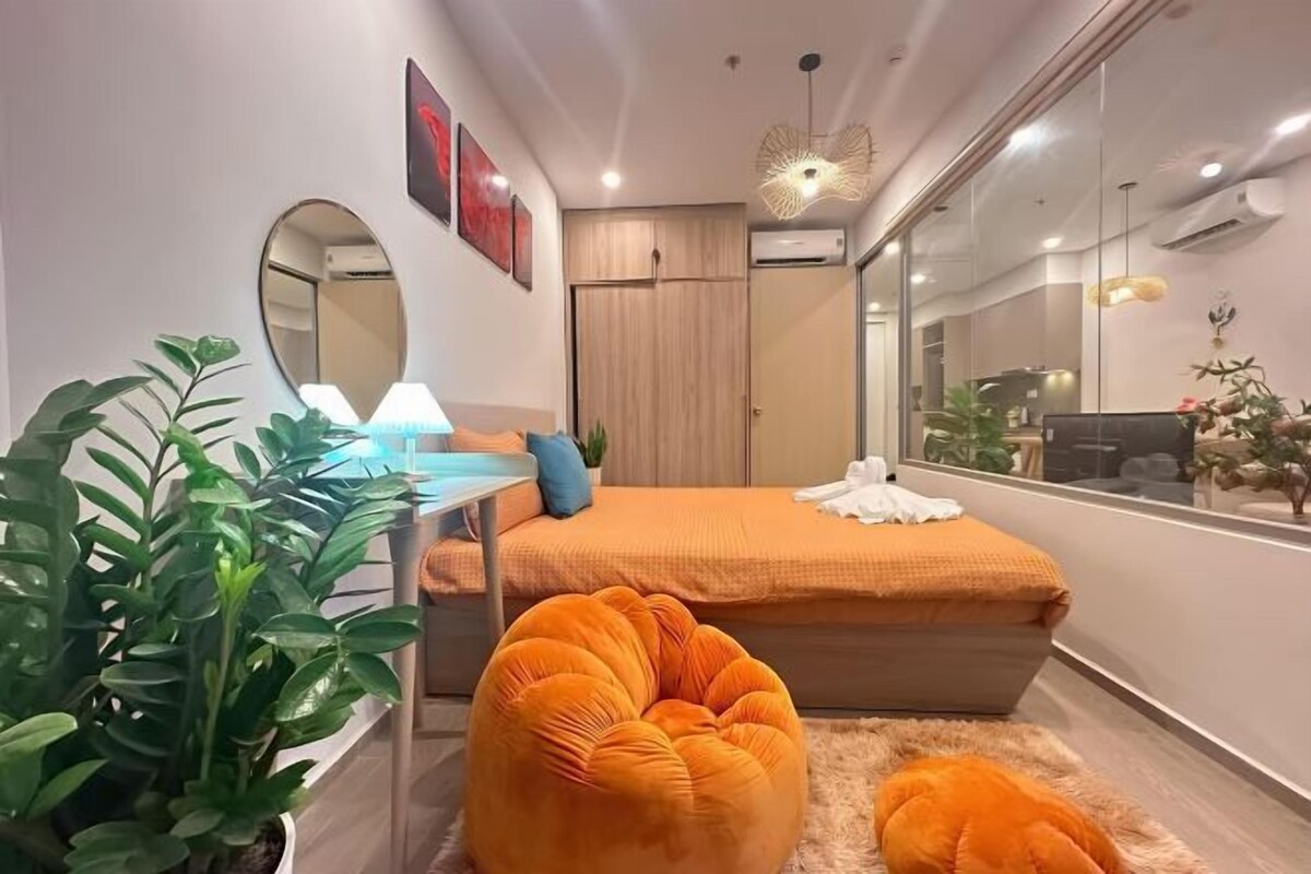 A modern bedroom with a bed, a desk, a mirror, and a potted plant.