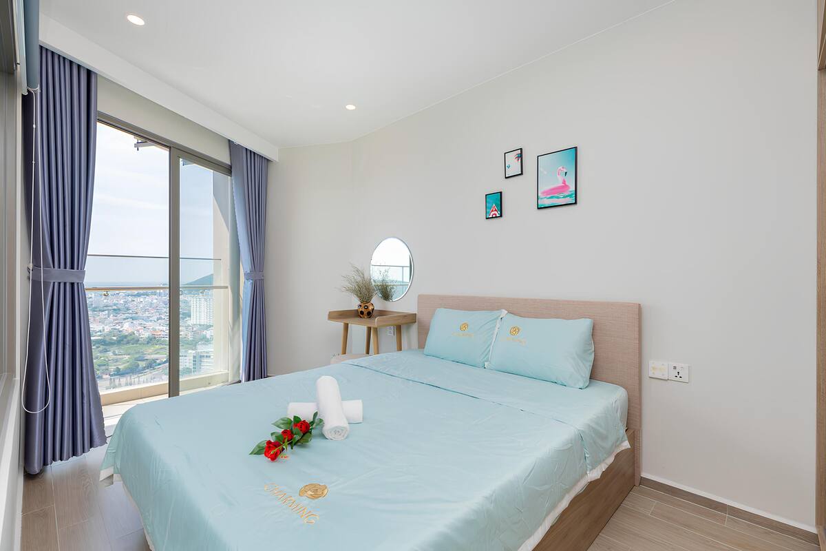 A bedroom with a large bed, a view of the city, and a small table with a vase.