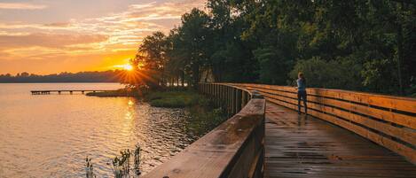 A wooden boardwalk by a lake at sunset.