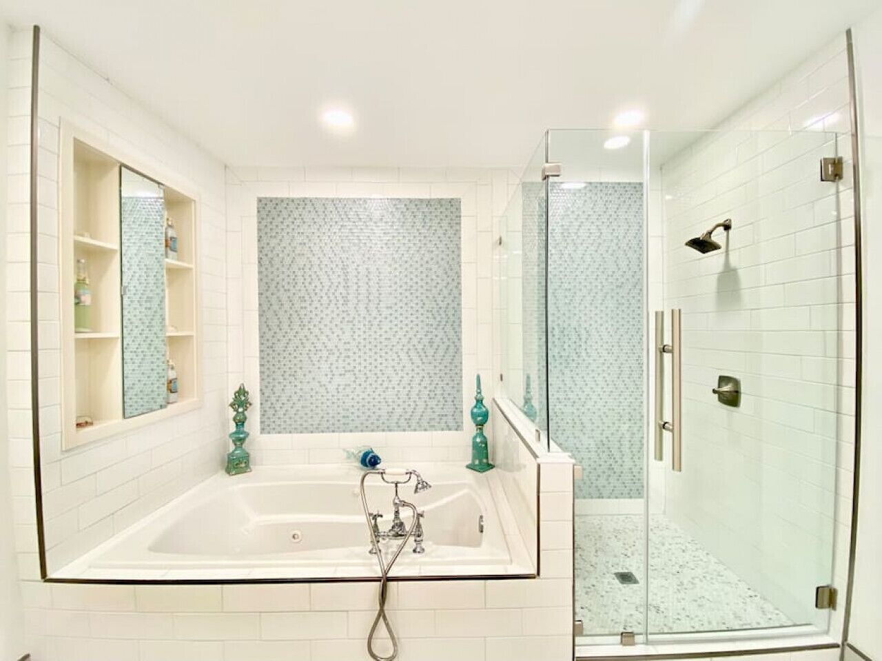 A bathroom with a large bathtub, a glass shower enclosure, and a mirrored vanity with shelves.