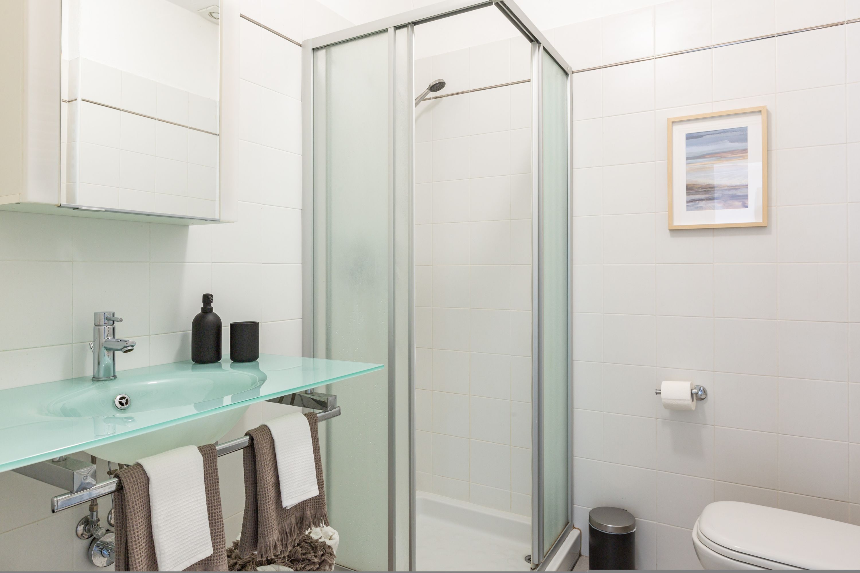A modern bathroom with a glass shower enclosure, a glass sink, and a toilet.