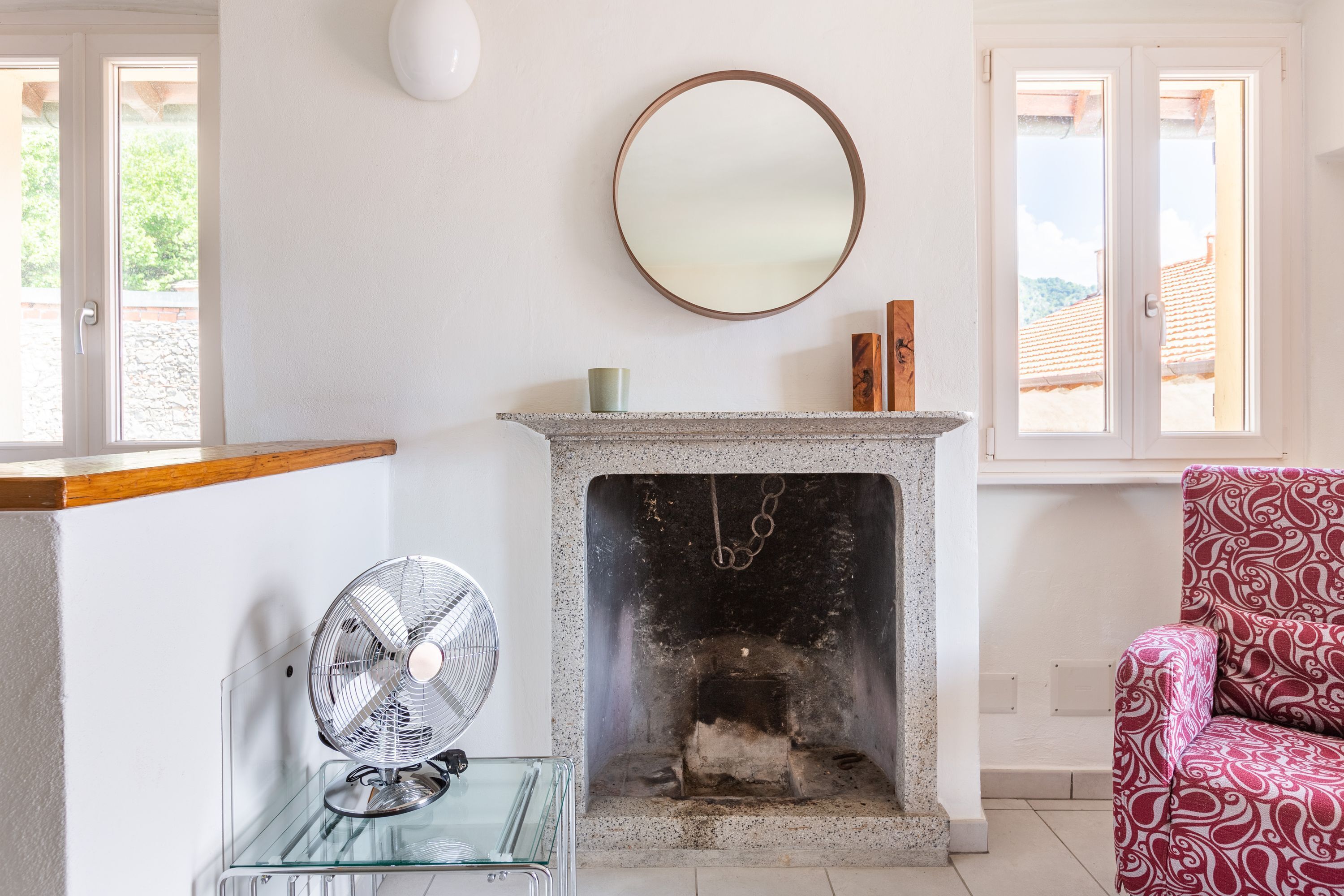 Una habitación con chimenea, un espejo, un ventilador y una silla estampada.