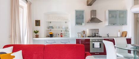 Une cuisine moderne avec des meubles blancs, une table à manger en verre et un canapé rouge agrémenté de coussins décoratifs.