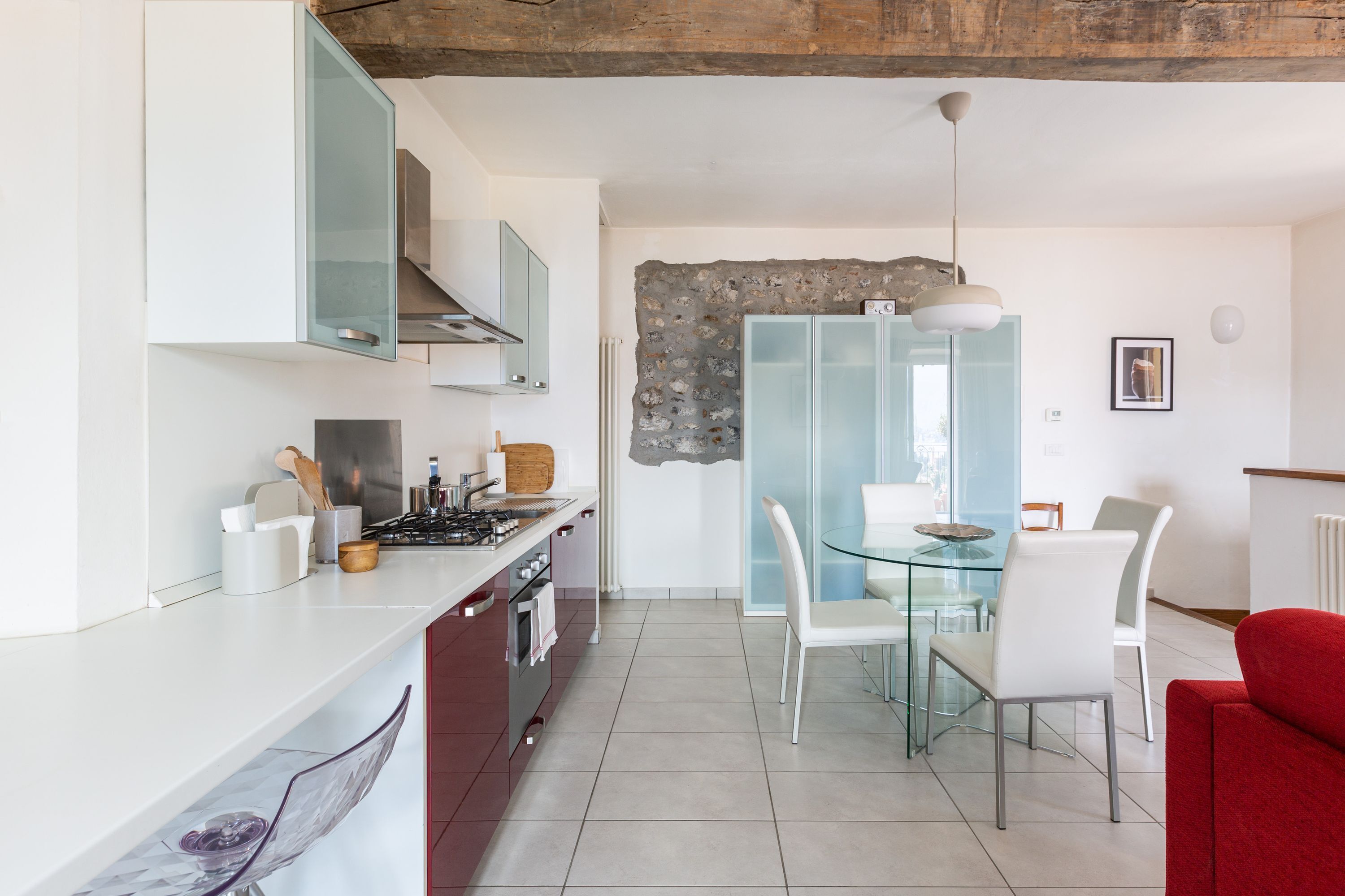 Una cocina moderna con armarios blancos, una estufa a gas y un comedor con mesa de vidrio y sillas blancas.
