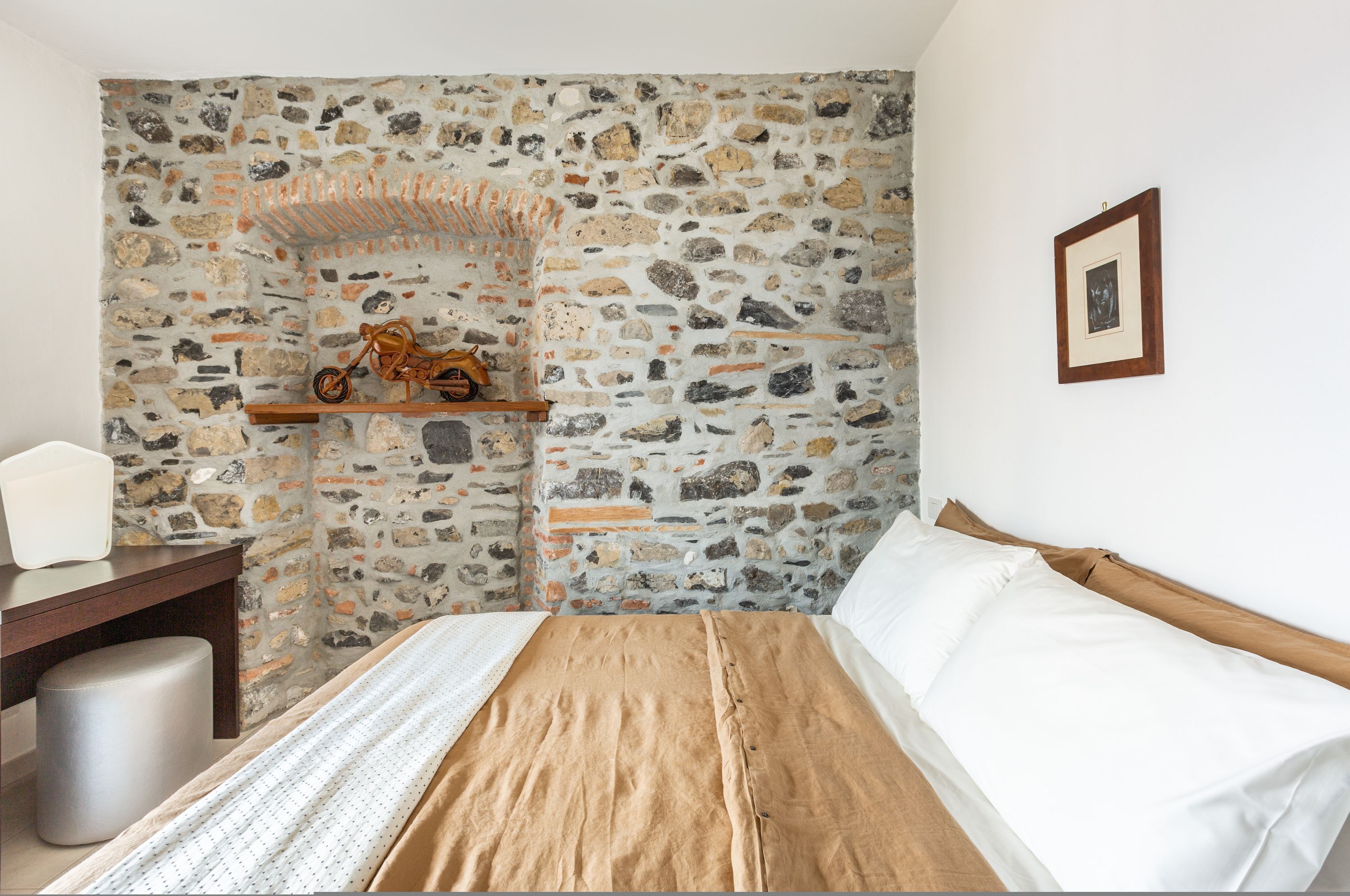 Ein Schlafzimmer mit Steinwand, einem hölzernen Bett, einem Nachttisch und einem gerahmten Bild an der Wand.