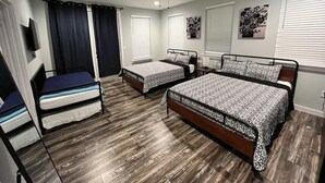 A bedroom with two single beds, a larger double bed, a ceiling fan, and a TV mounted on the wall.