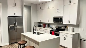A modern kitchen with white cabinetry, stainless steel appliances, and a central island with stools.