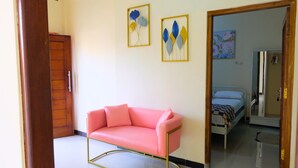 A room with a pink sofa, a wooden wardrobe, and two framed artworks on the wall. - Alesya Homestay Syariah (Yogyakarta)