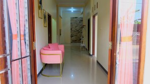 A hallway with a pink sofa, a stone wall, and a white ladder. - Alesya Homestay Syariah (Yogyakarta)