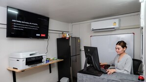 A small office with a desk, computer, printer, refrigerator, and a TV displaying a Netflix ad. - Delta 9 Hostel (Bangkok)