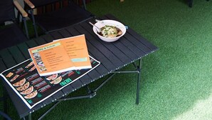 A restaurant interior with a neon 'OPEN' sign, a chalkboard menu, and a seating area with tables and chairs. - Delta 9 Hostel (Bangkok)