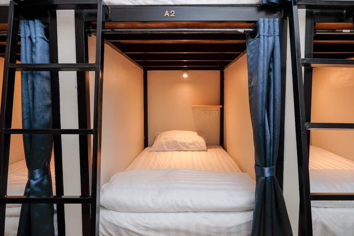 A bunk bed room with a white mattress, a single pillow, and a small shelf above the bed.