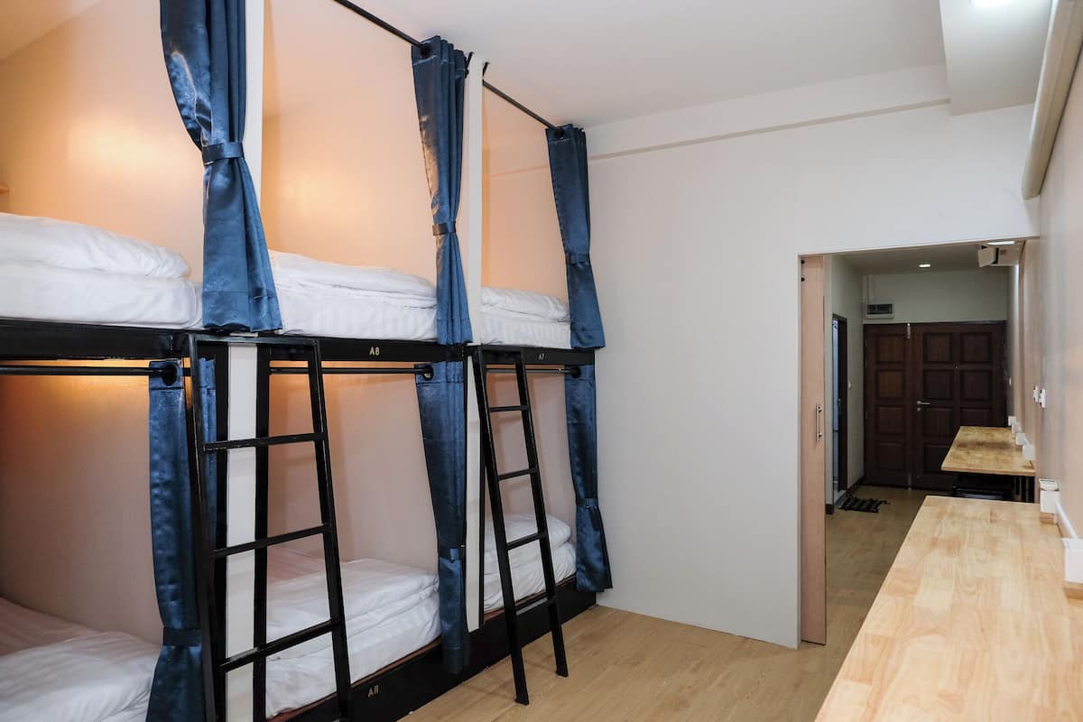 A bunk bed room with a wooden floor, a desk, and a door leading to a kitchen area.