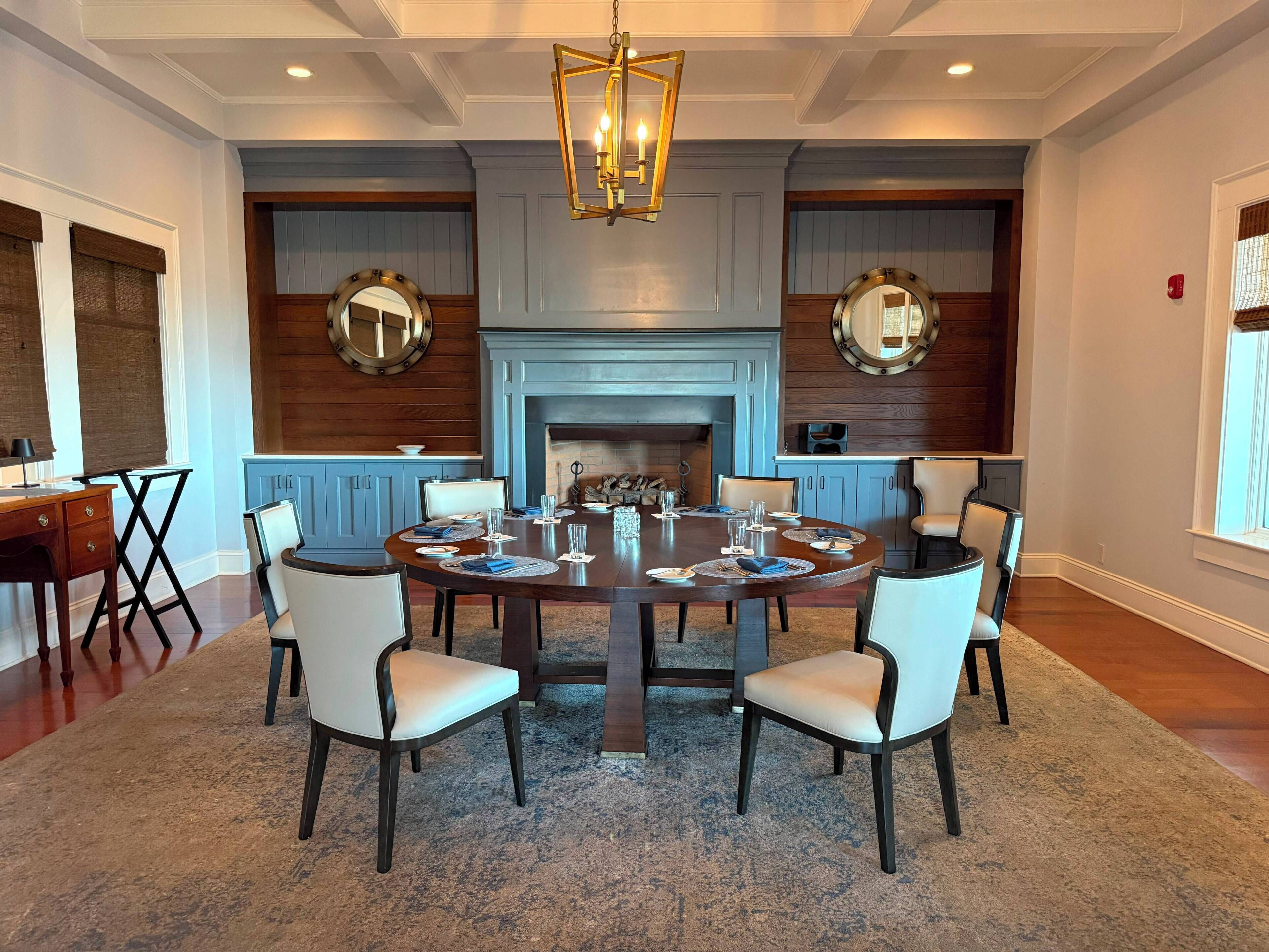 A conference room with a round table, chairs, a fireplace, and decorative mirrors.
