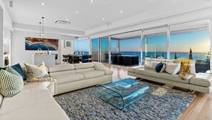 Sala de estar moderna com dois sofás, uma mesa de centro de vidro e uma janela grande com vista para o oceano.