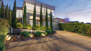 Uma casa moderna de dois andares com fachada de pedra, grandes janelas e um jardim bem cuidado com ciprestes e suculentas.