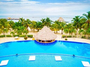 A large, clear blue pool with a central bar area, surrounded by palm trees and a beach view. - Villa Castello, Private, Amenities, Walk to Beach (Placencia)