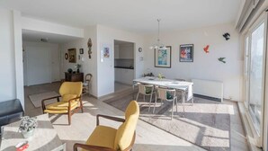 Amplia sala de estar con una mesa de comedor, dos sillones amarillos, un sofá y un amplio ventanal que proporciona luz natural.