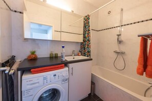 Une petite salle de bain équipée d’un lave-linge, d’un évier et d’une douche.