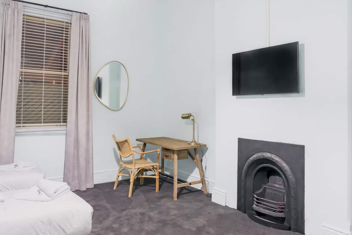 Een slaapkamer met een bed, een bureau met stoel, een spiegel, een open haard en een televisie aan de muur.