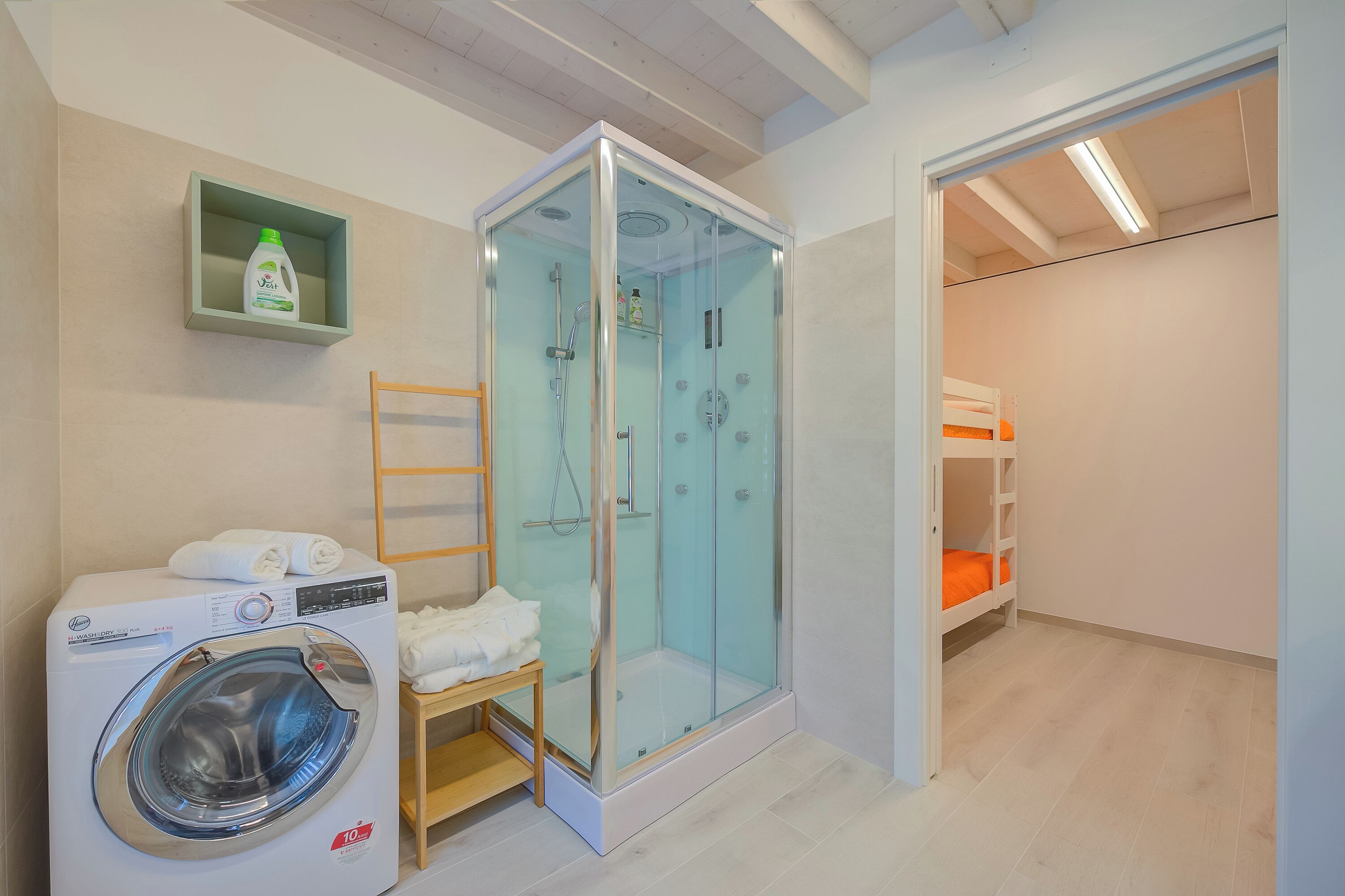 Un baño moderno con ducha de vidrio, lavadora y estante con artículos de aseo.