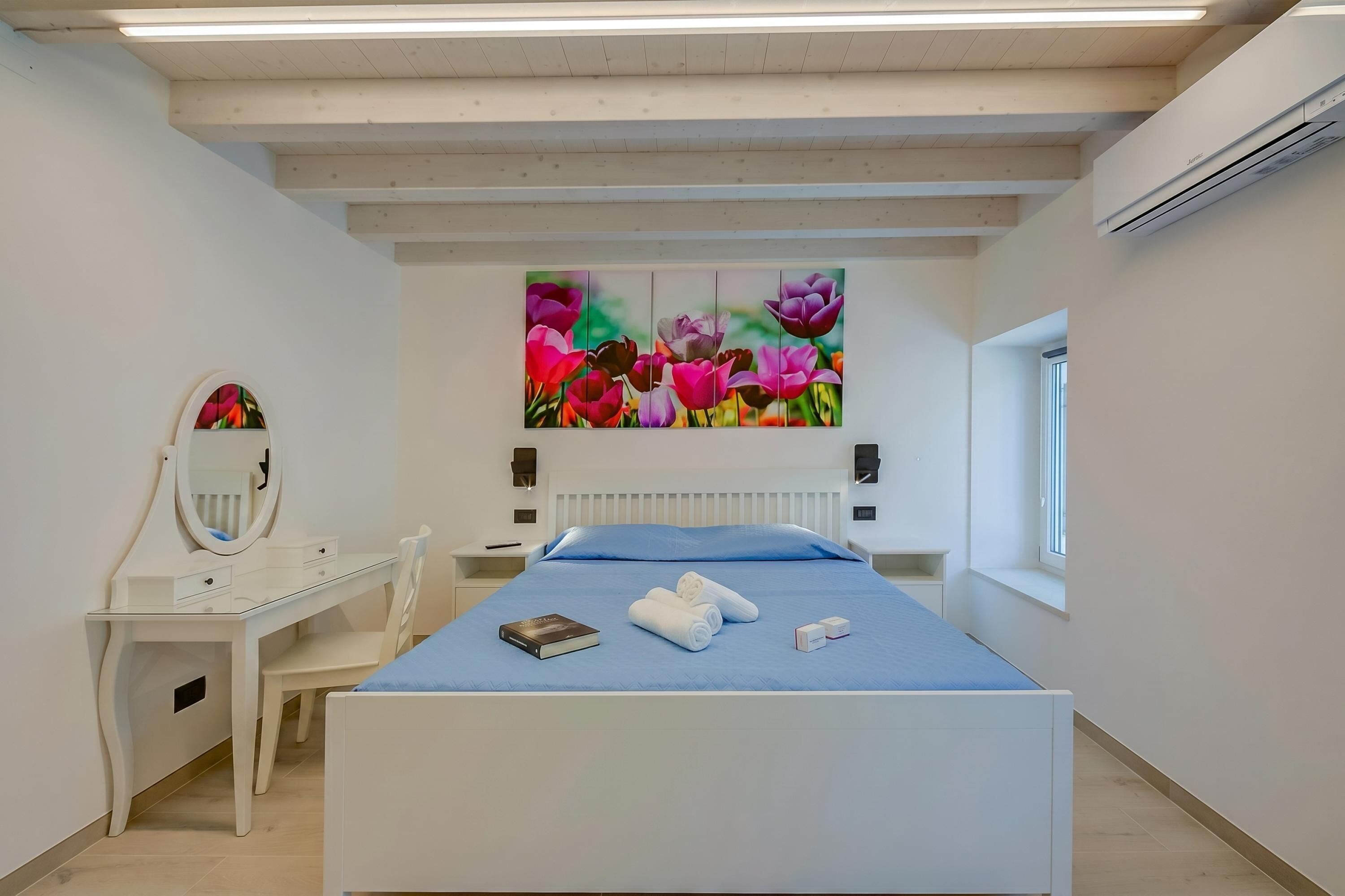 Een slaapkamer met een bed, een bureau, een stoel, een spiegel, een raam en een radiator aan de muur.