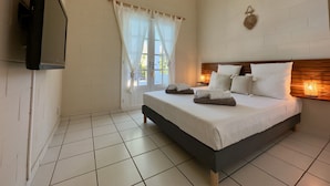 Une chambre à coucher comprenant un lit, un téléviseur fixé au mur, une fenêtre avec des rideaux et un luminaire fixé au mur.