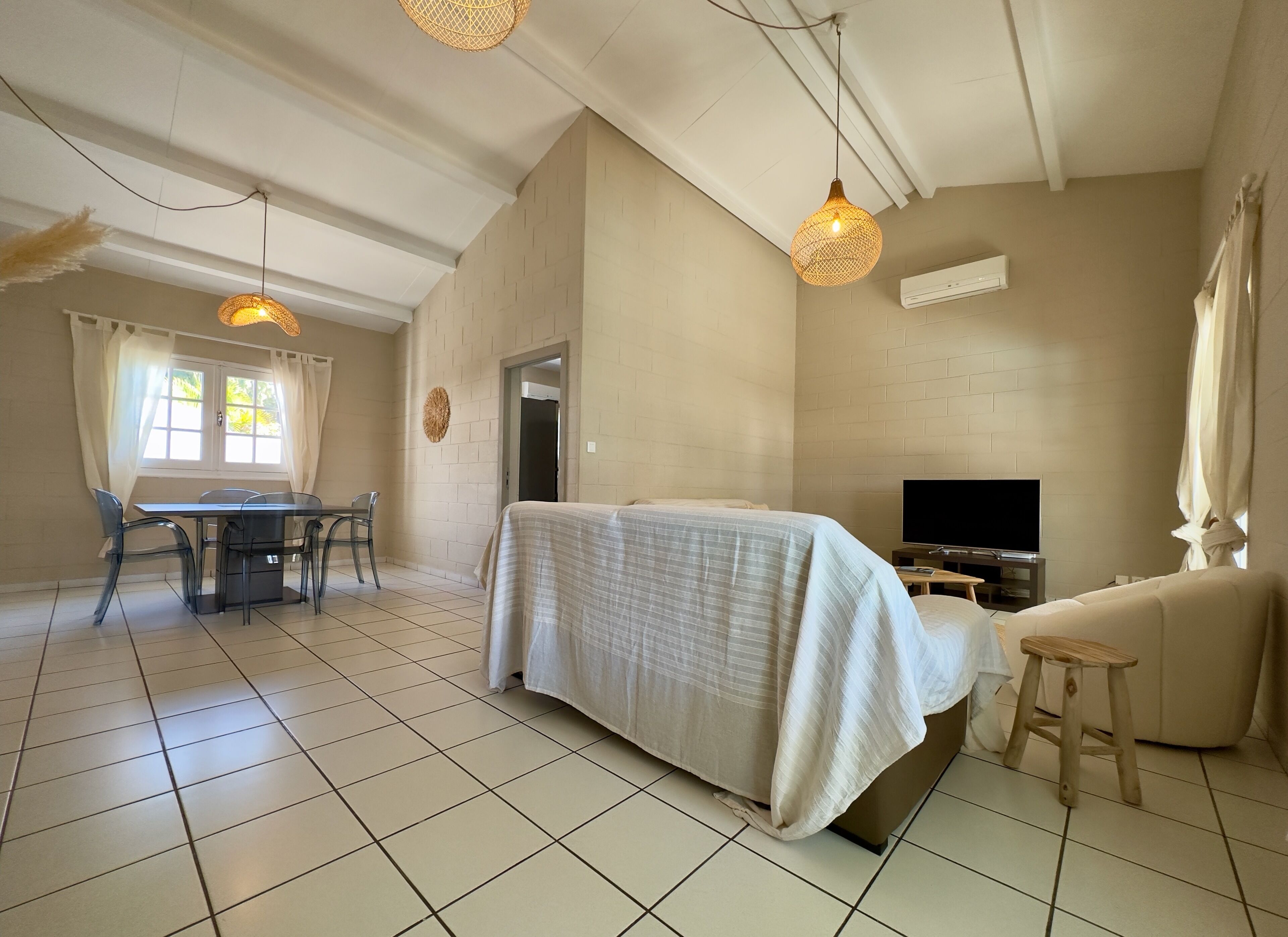 A hotel room with a bed, a TV, a dining table with chairs, and a balcony with curtains.