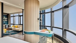 Ein modernes Hotelzimmer mit einem gewölbten Schreibtisch, einer großen Holzsäule und Blick auf die Stadt.