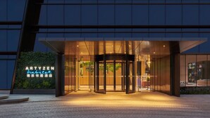 Ein moderner Hotelzugang mit einer Doppeltür, einer Neonreklame und einer Glasfassade.