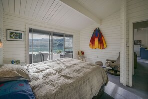 A bedroom with a large bed, a view of the outdoors, a colorful umbrella, and a small table with chairs. - Birdsong Bliss - Takamatua Holiday Home (Takamatua)
