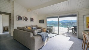 Ein modernes Wohnzimmer mit einer Couch, einem Fernseher und einer großen Schiebeglastür, die auf einen Balkon mit schöner Aussicht führt.