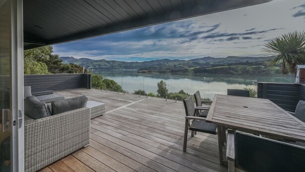 Eine Terrasse mit einer Rattan-Couch und einem Tisch, mit Blick auf einen See und Berge.