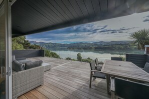 A deck with a wicker sofa and a table, overlooking a lake and mountains. - Birdsong Bliss - Takamatua Holiday Home (Takamatua)