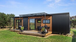 A modern, compact house with a patio area, large sliding glass doors, and a black exterior. - Peace in Paradise - Tokerau Beach Holiday Home (Tokerau Beach)