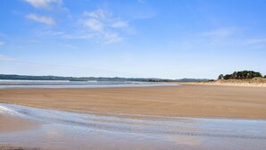 A wide sandy beach with gentle waves, a clear sky, and distant hills. - Peace in Paradise - Tokerau Beach Holiday Home (Tokerau Beach)
