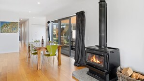Ein modernes Wohnzimmer mit einem schwarzen Kaminofen, einem Esstisch mit Stühlen und einem großen Fenster mit Vorhängen.