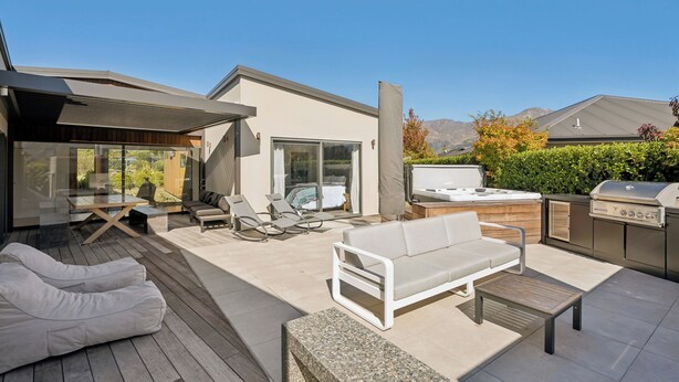 Eine moderne Terrassenanlage mit weißer Couch, Liegestühlen, einem Esstisch und einem Grill.