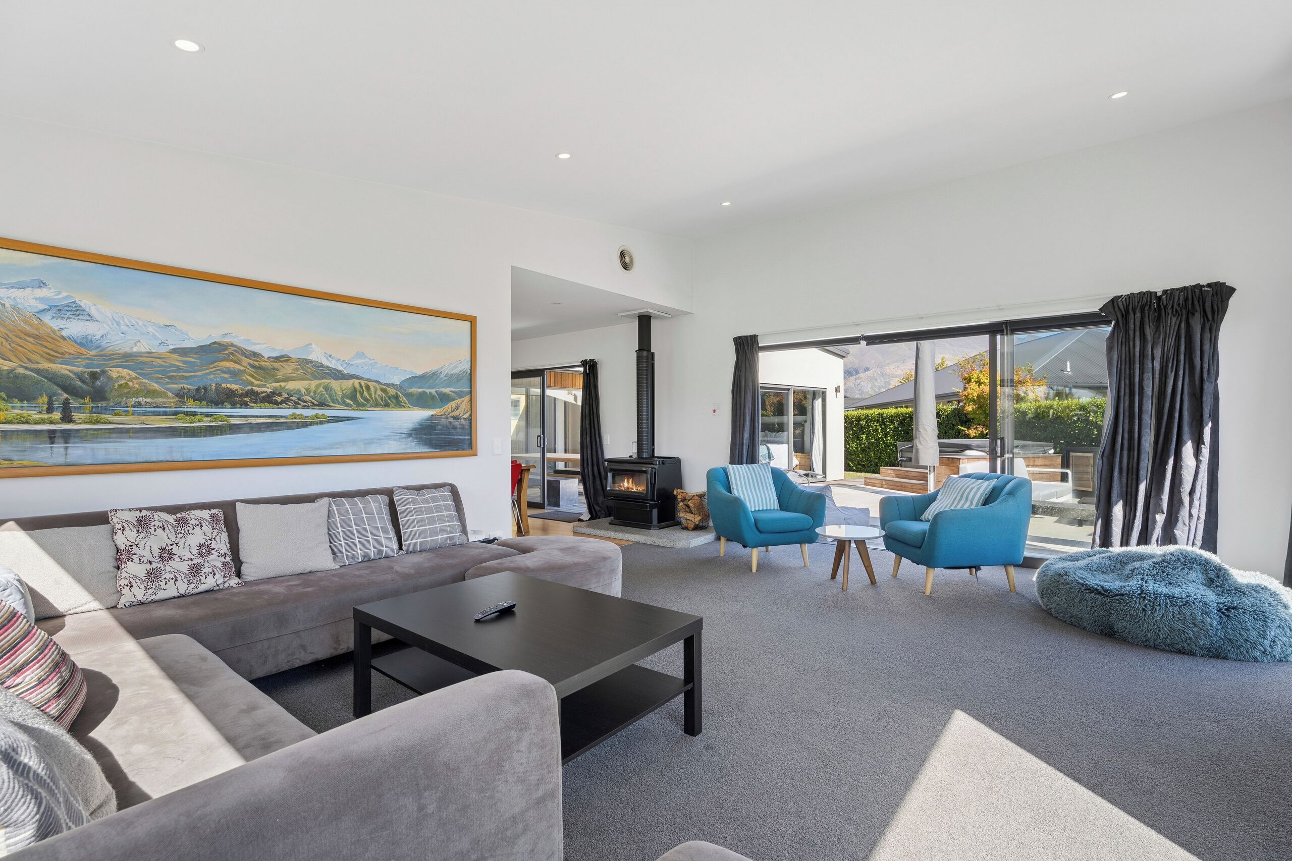A modern living room with a sofa, armchairs, a coffee table, a fireplace, and a large window with a view of mountains and a lake.