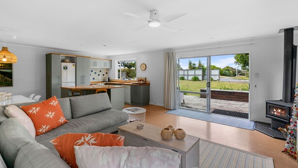 A modern living room with a grey sofa, a coffee table, and a fireplace. There is a kitchen in the background with a dining table and chairs.