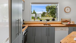 A modern kitchen with grey cabinets, a wooden countertop, a stainless steel sink, and a Bosch dishwasher.