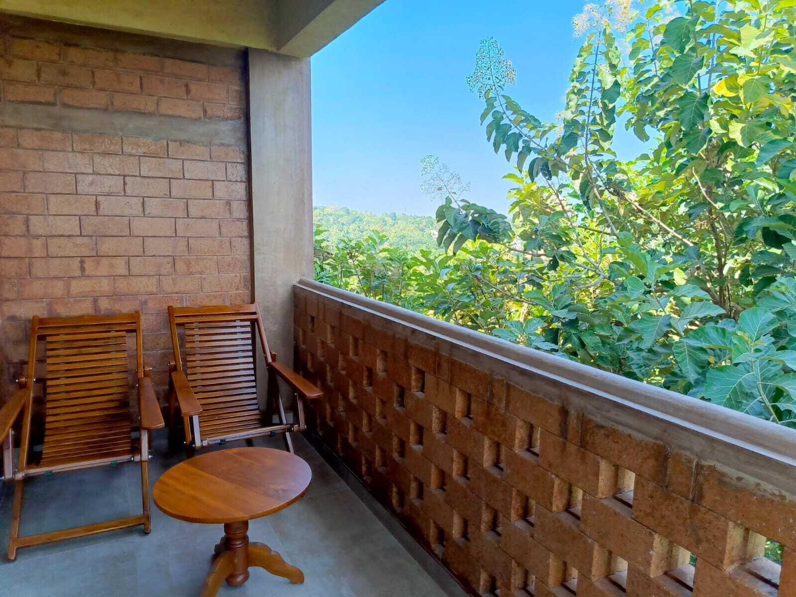 A balcony with a brick wall, two wooden chairs, a small round table, and a view of greenery.