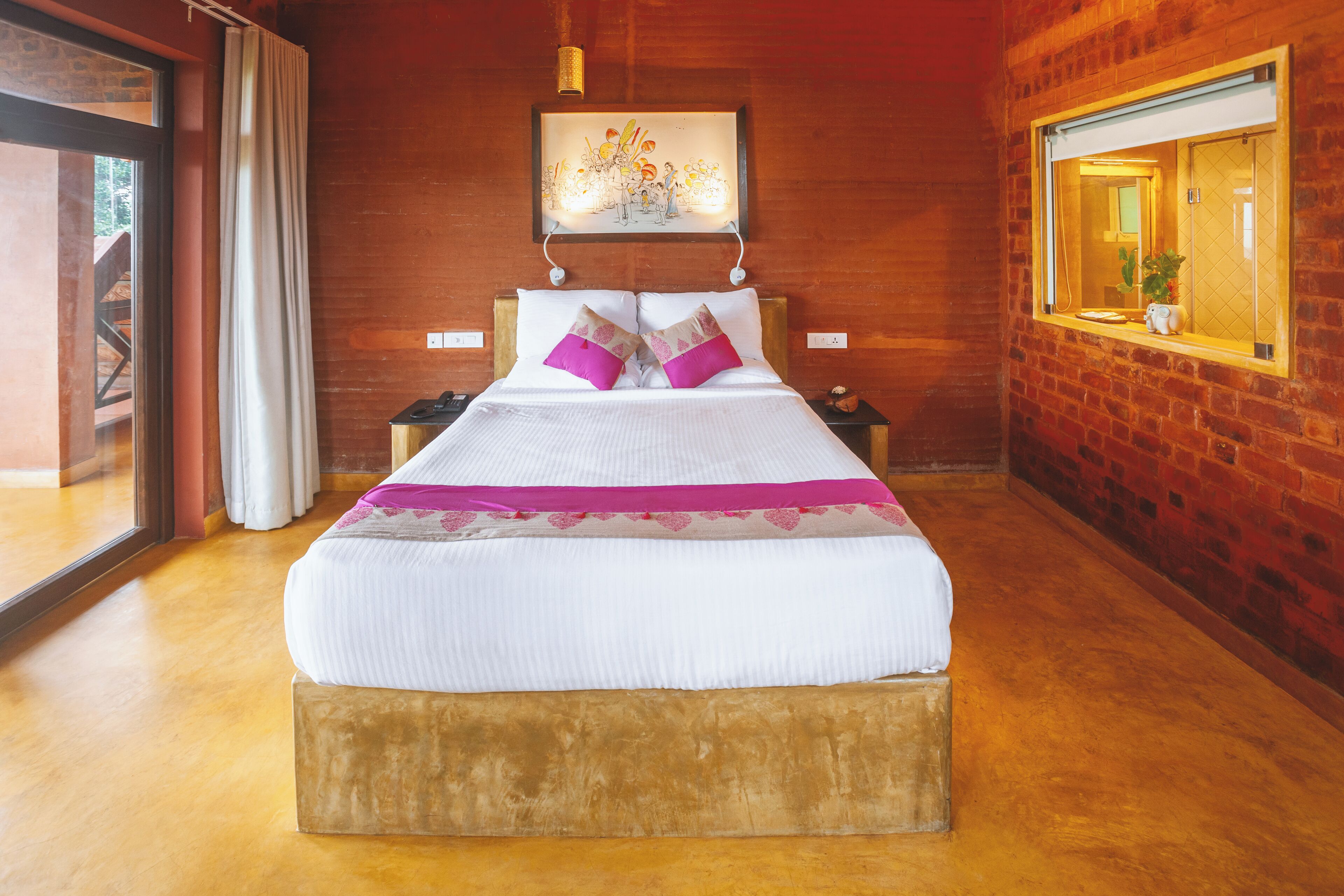 Ein großes Bett mit Holz Kopfteil, ein Nachttisch, ein Beistelltisch und ein Fenster mit Blick ins Freie.