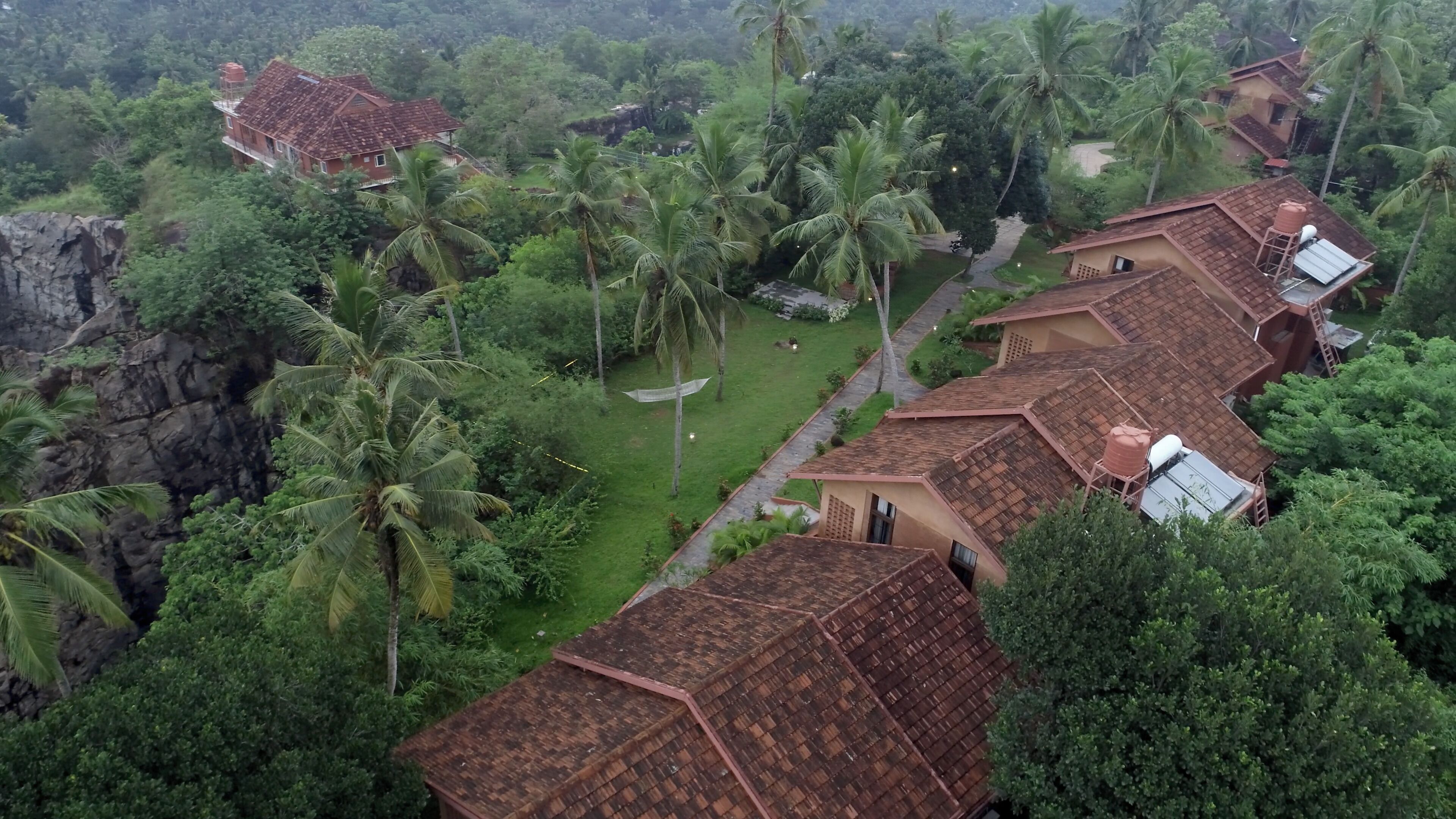 A residential area with multiple houses featuring red-tiled roofs, surrounded by lush greenery and palm trees.