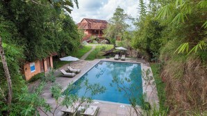 Una piscina rodeada de exuberante vegetación, con un edificio pequeño y una escalera que lleva a una casa al fondo.