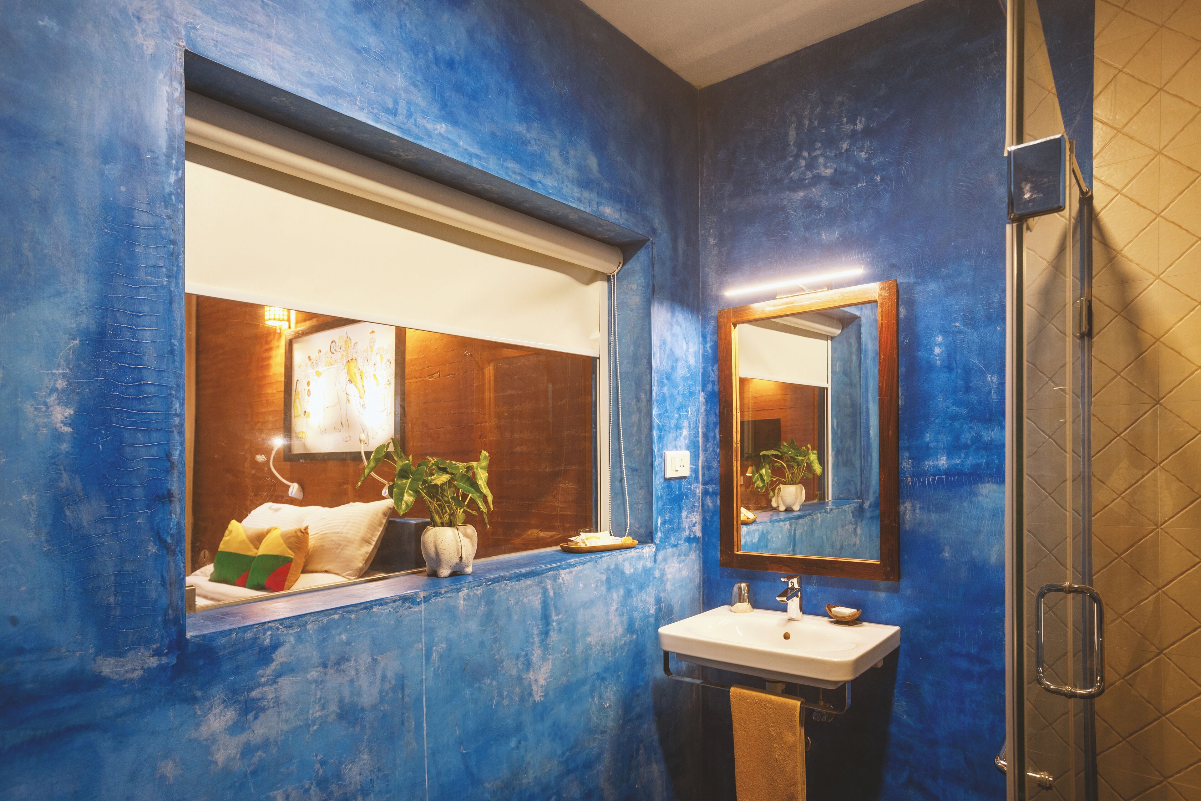 A bathroom with a blue wall, a window with a view, a sink, and a mirror.