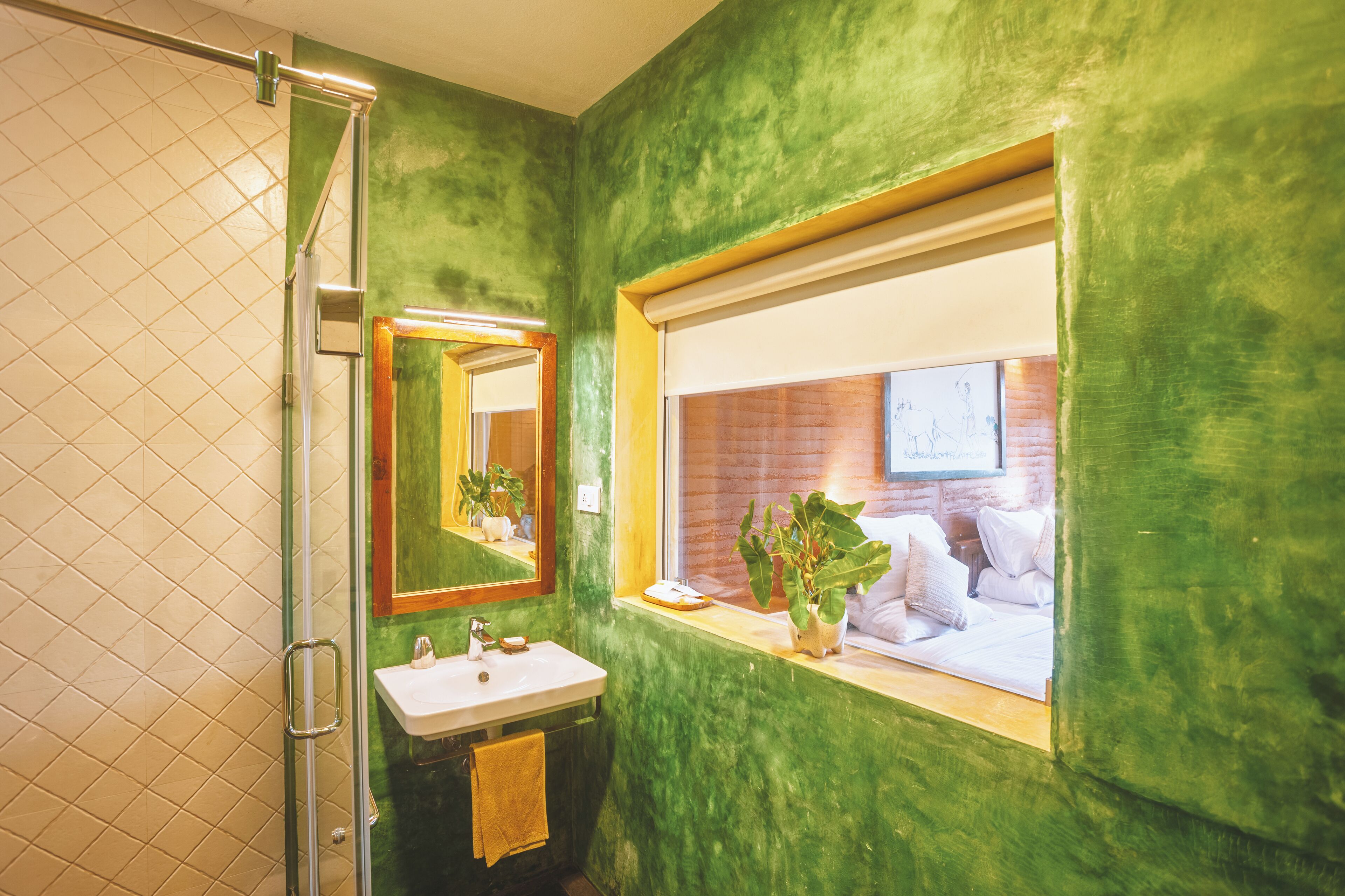 Un baño con pared verde, una ventana con vista a un muro de ladrillo, un lavabo y un espejo.
