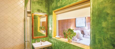 Un baño con pared verde, una ventana con vista a un muro de ladrillo, un lavabo y un espejo.