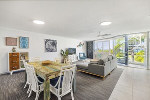 Relax in a spacious living area with a dining table, sofa, and side table, offering a view of the staircase and lush greenery outside.